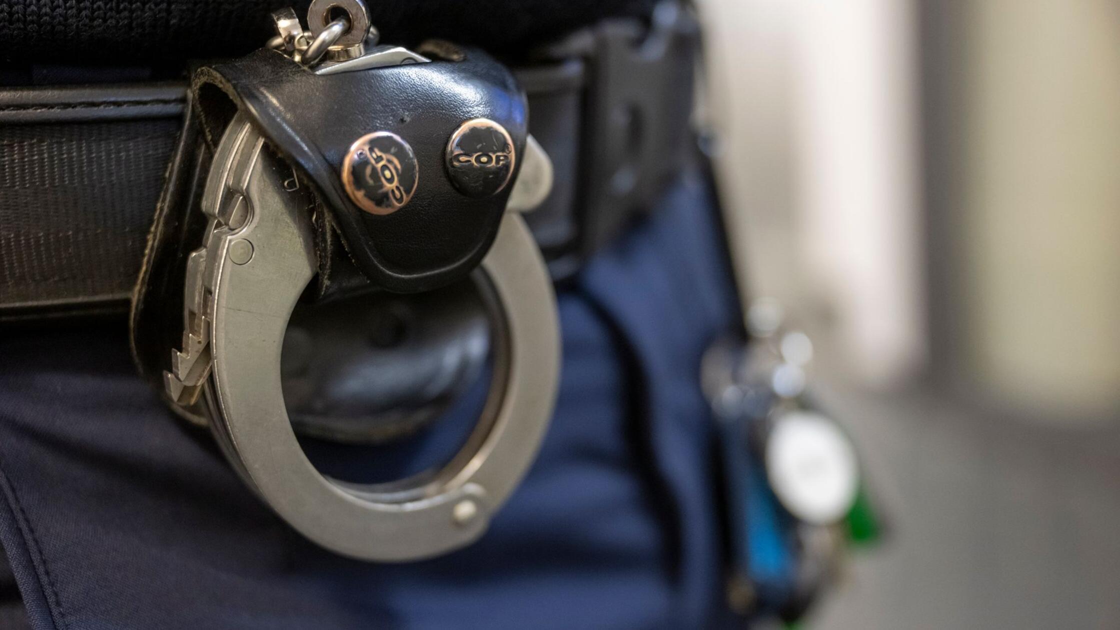 Eine Handschelle hängt am Gürtel eines Polizisten.