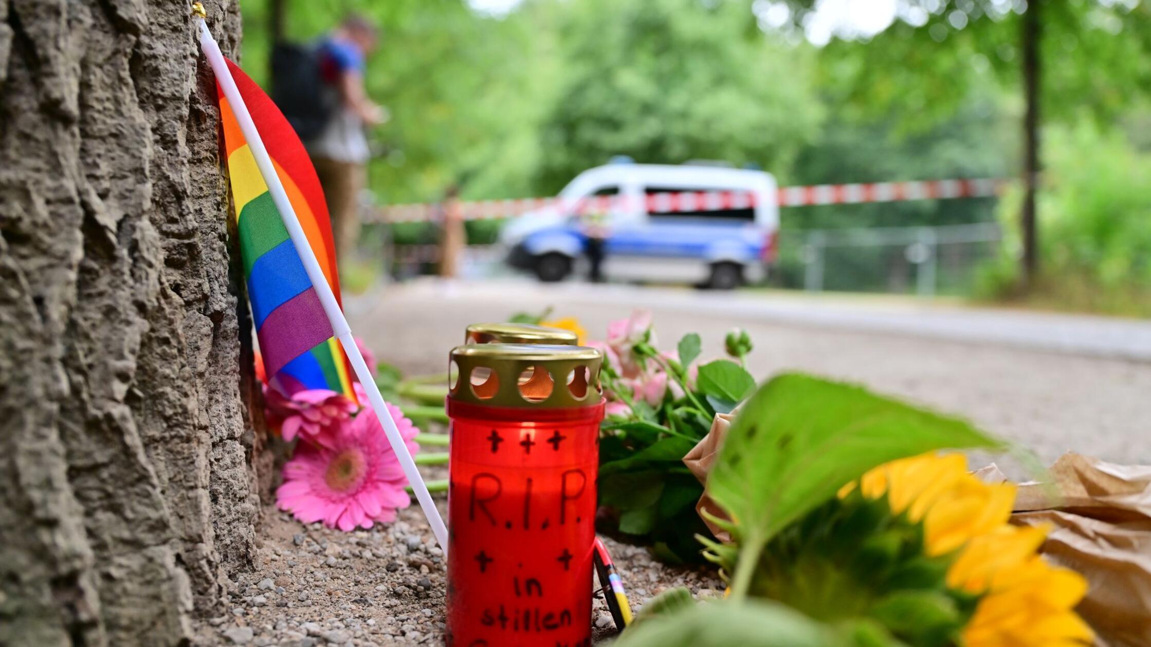 Eine Regenbogenflagge, Blumen und Kerzen stehen vo