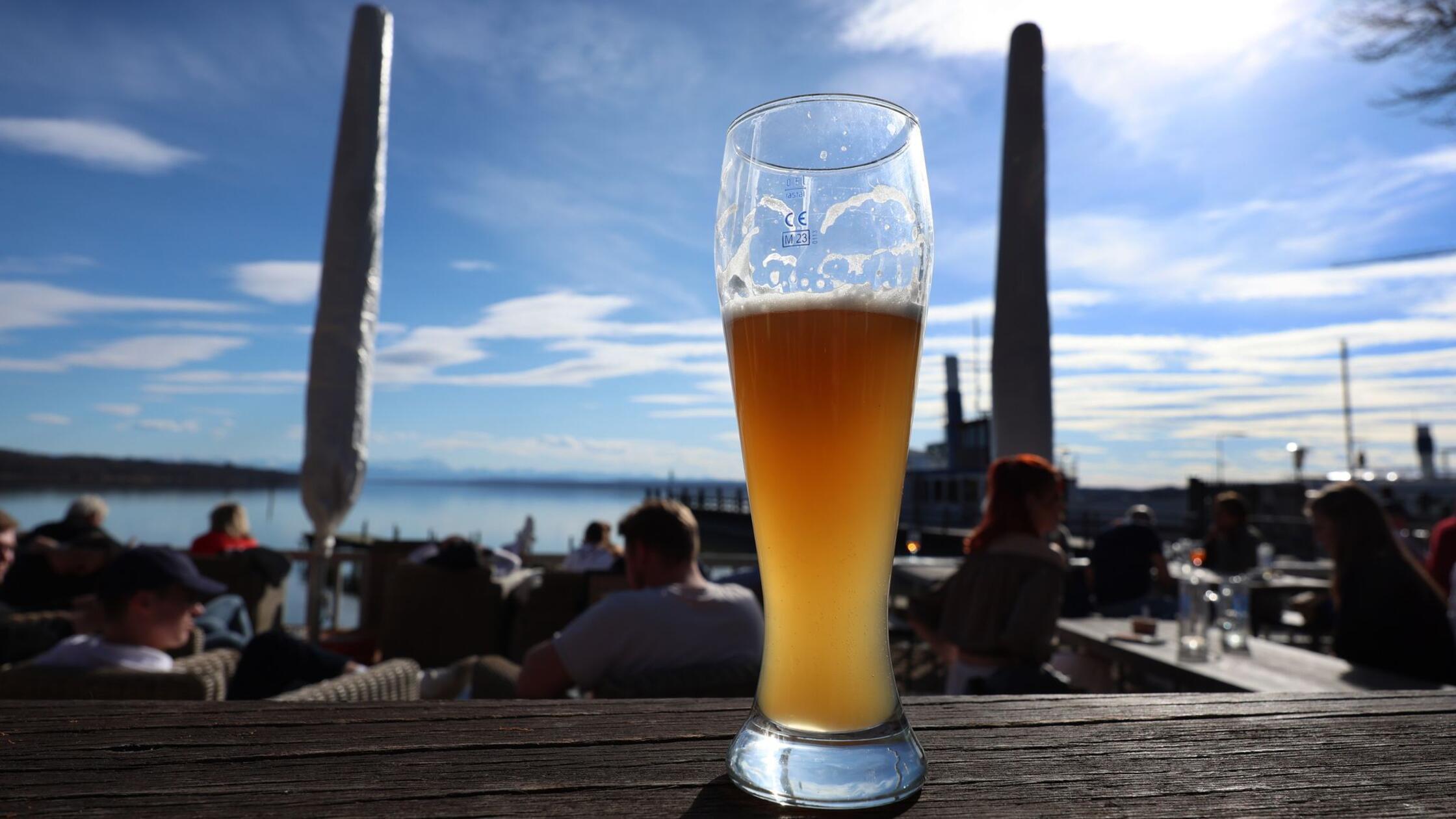Ein Glas mit Weizenbier steht in einem Biergarten 