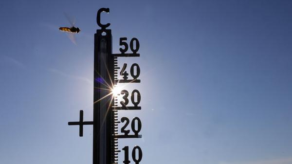 Die Sonne scheint hinter einem Thermometer, an dem