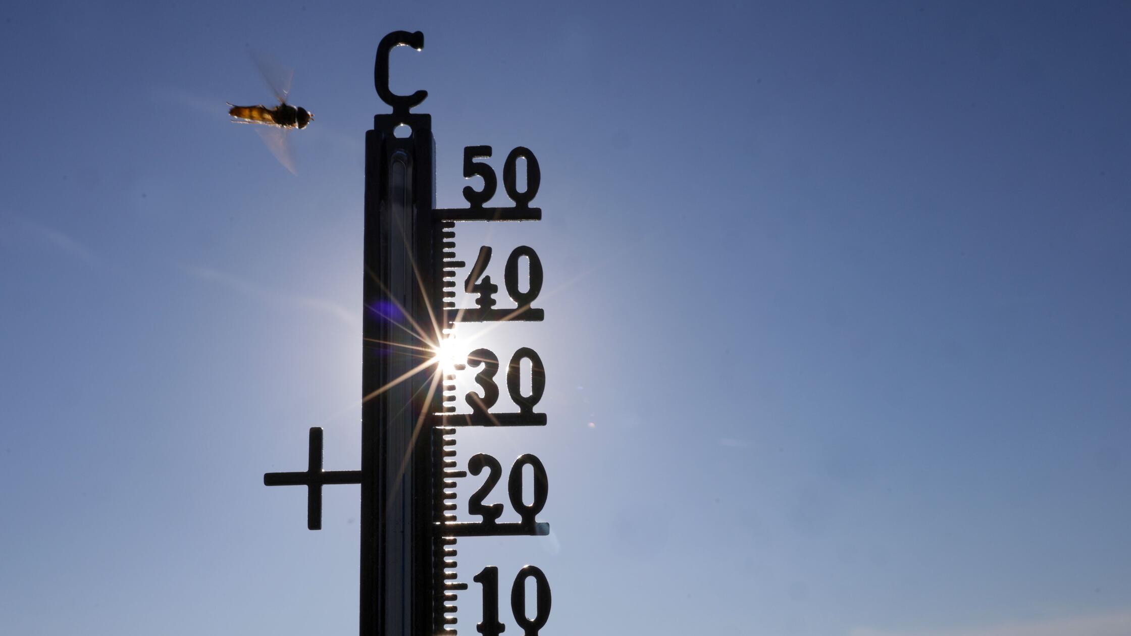 Die Sonne scheint hinter einem Thermometer, an dem