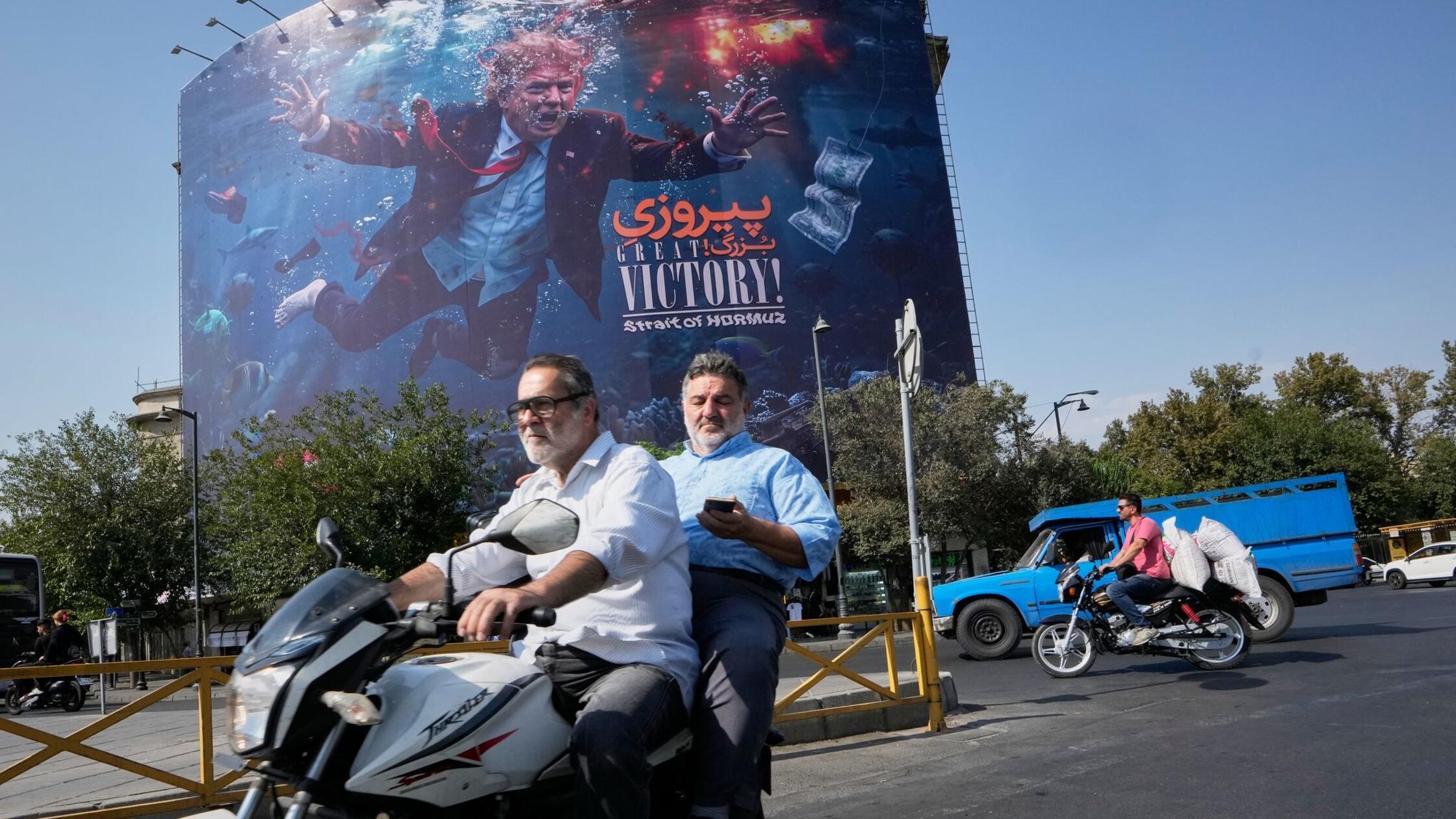 Motorradfahrer fahren an einer Plakatwand vorbei, 