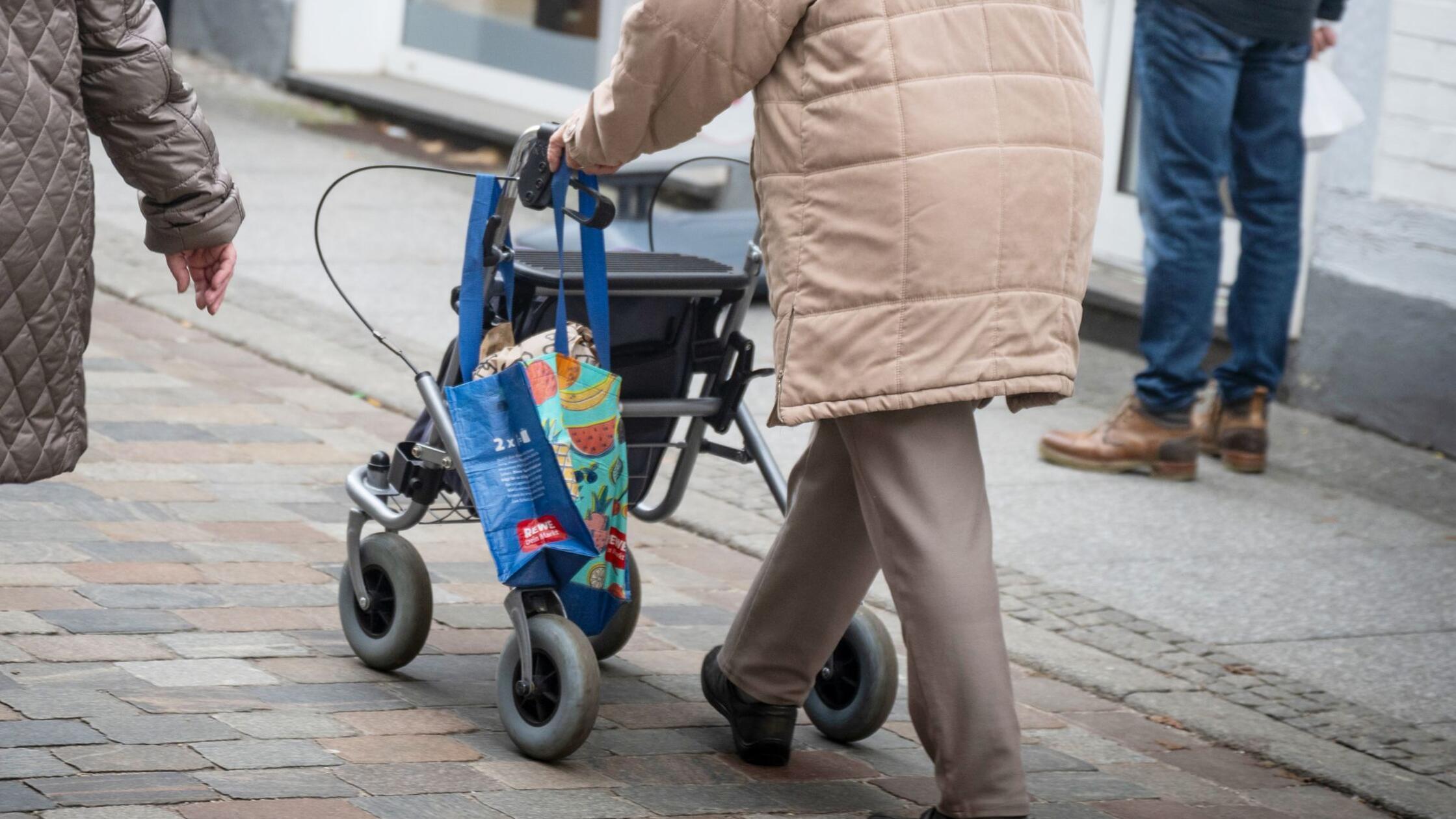 Eine Seniorin schiebt mit Einkaufstaschen an ihrem