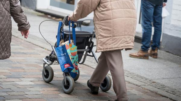 Eine Seniorin schiebt mit Einkaufstaschen an ihrem