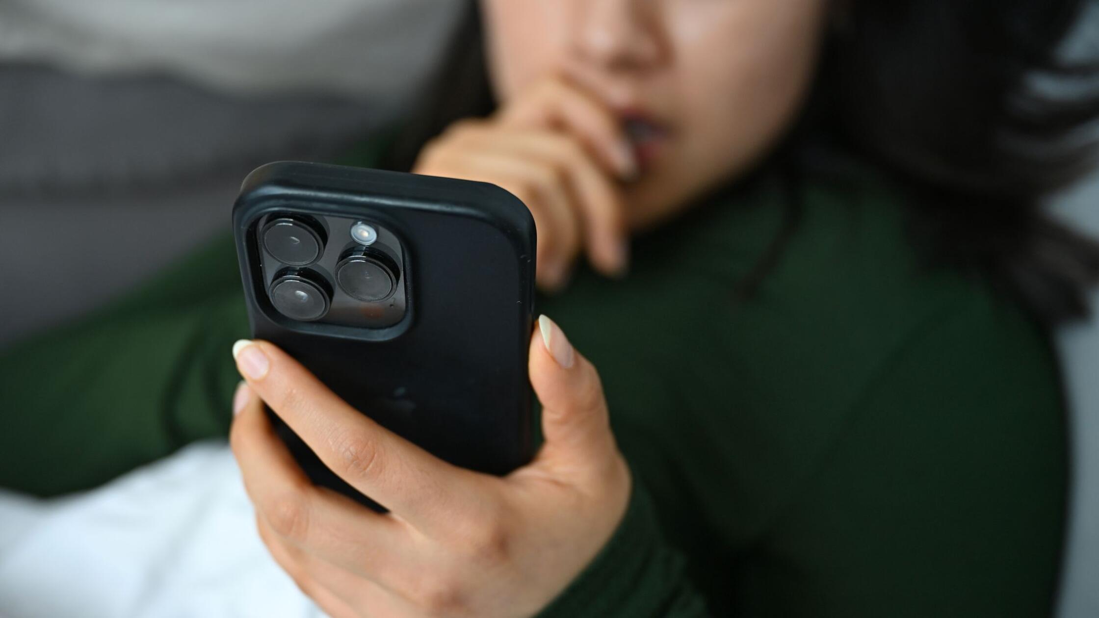 Eine junge Frau liegt mit ihrem Handy auf der Couc