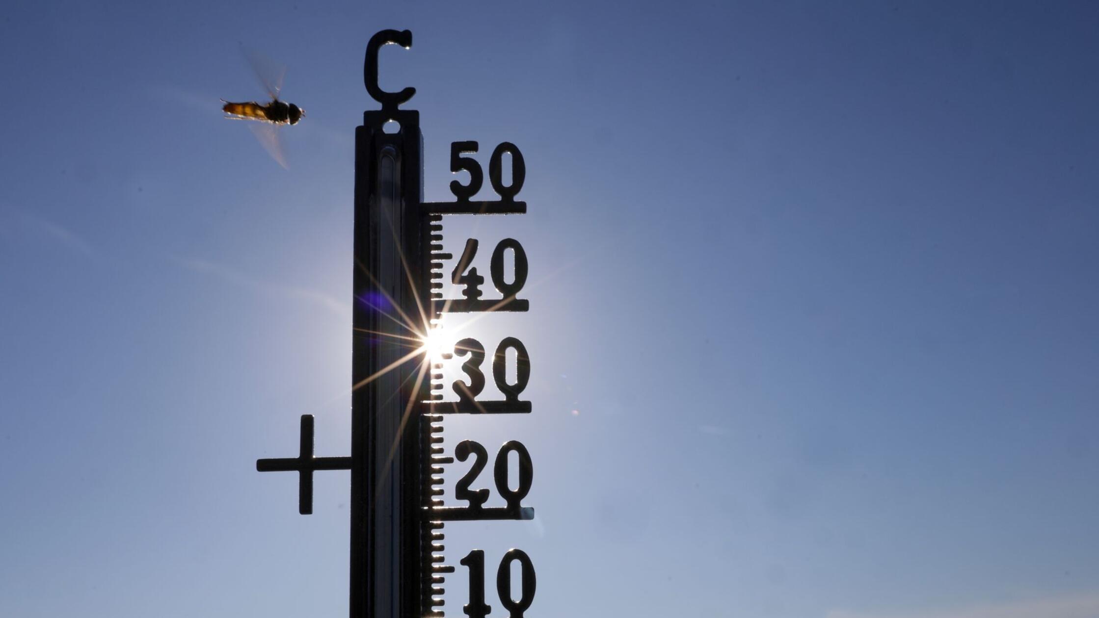 Die Sonne scheint hinter einem Thermometer, an dem