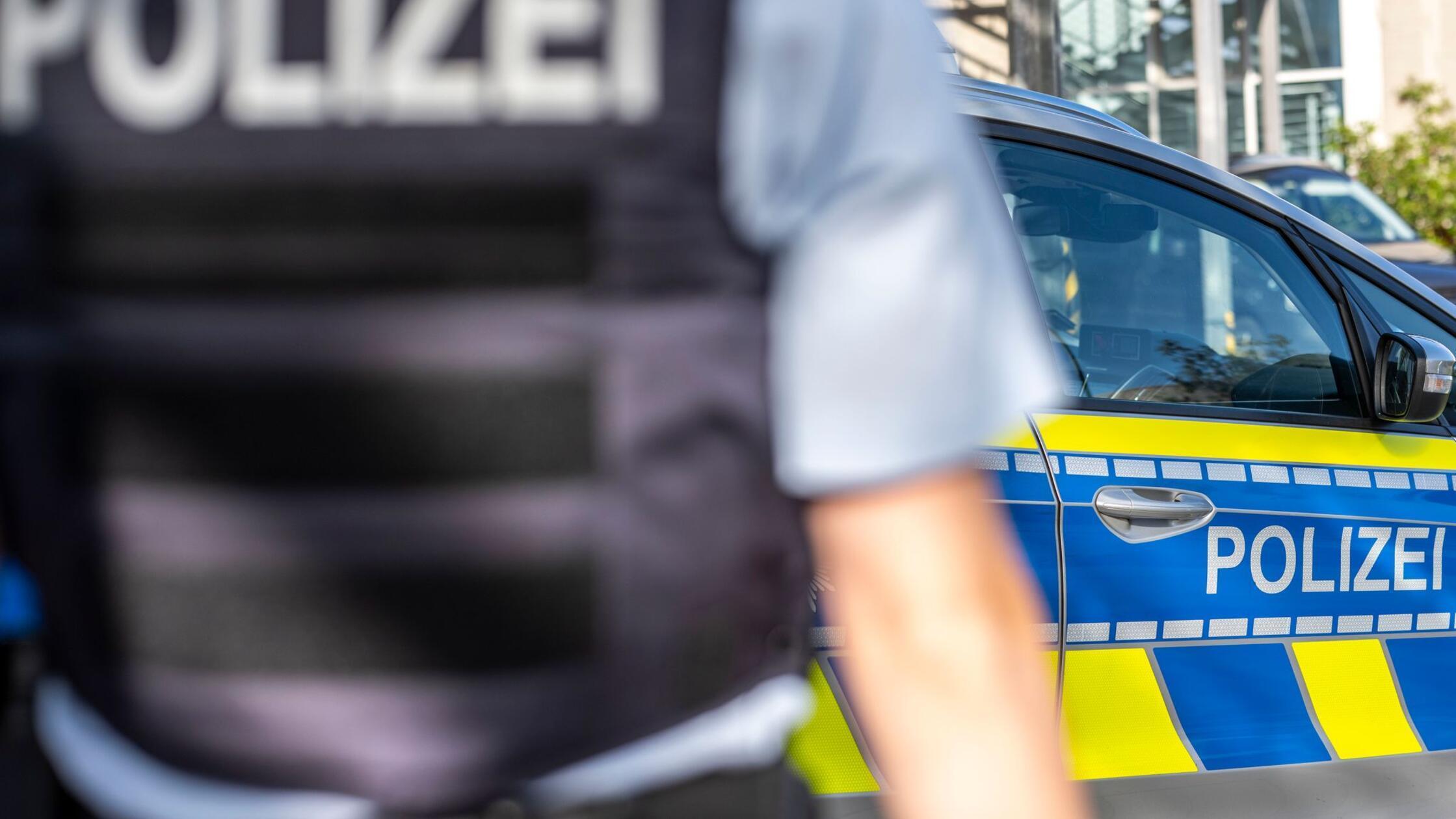 Ein Polizist steht vor einem Streifenwagen. Ermitt