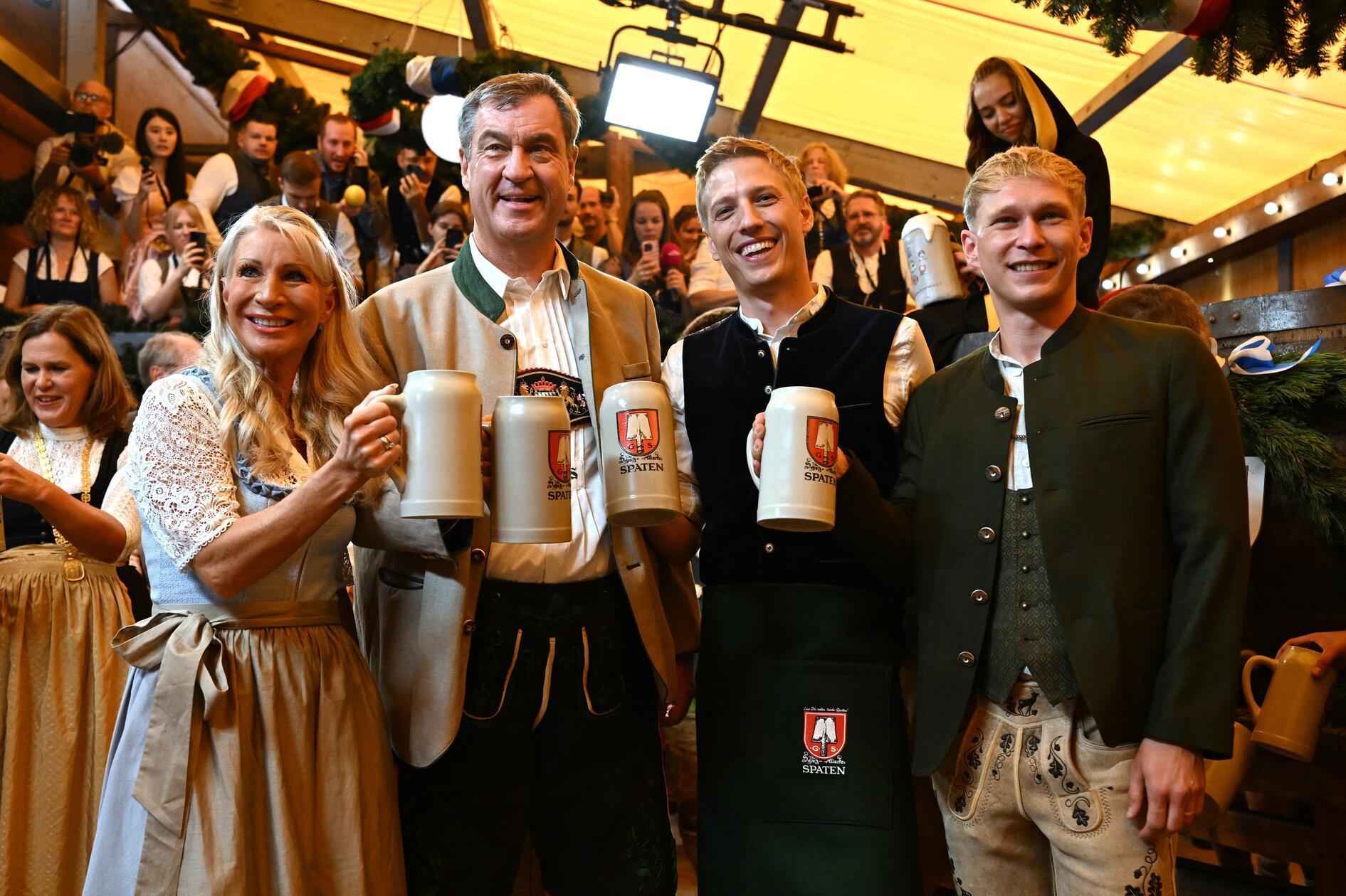 Karin Baumüller-Söder (l-r), Markus Söder (CSU), Ministerpräsident von Bayern, Dominik Krause (Bündnis 90/ Die Grünen), Oberbürgermeister von München, und sein Partner Sebastian Müller, stehen nach dem traditionellen Fassanstich in der Festhalle Schottenhamel mit Maßkrügen nebeneinander. 