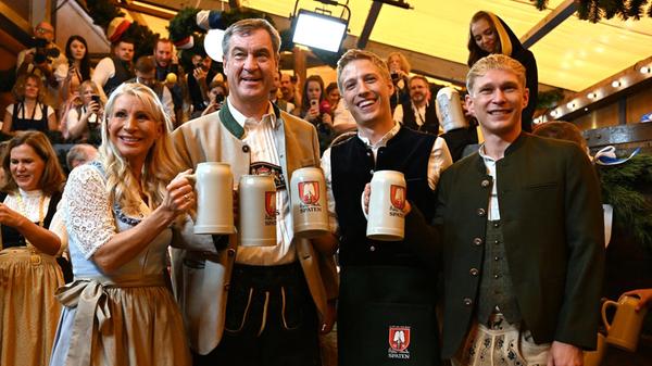 Karin Baumüller-Söder (l-r), Markus Söder (CSU), Ministerpräsident von Bayern, Dominik Krause (Bündnis 90/ Die Grünen), Oberbürgermeister von München, und sein Partner Sebastian Müller, stehen nach dem traditionellen Fassanstich in der Festhalle Schottenhamel mit Maßkrügen nebeneinander.