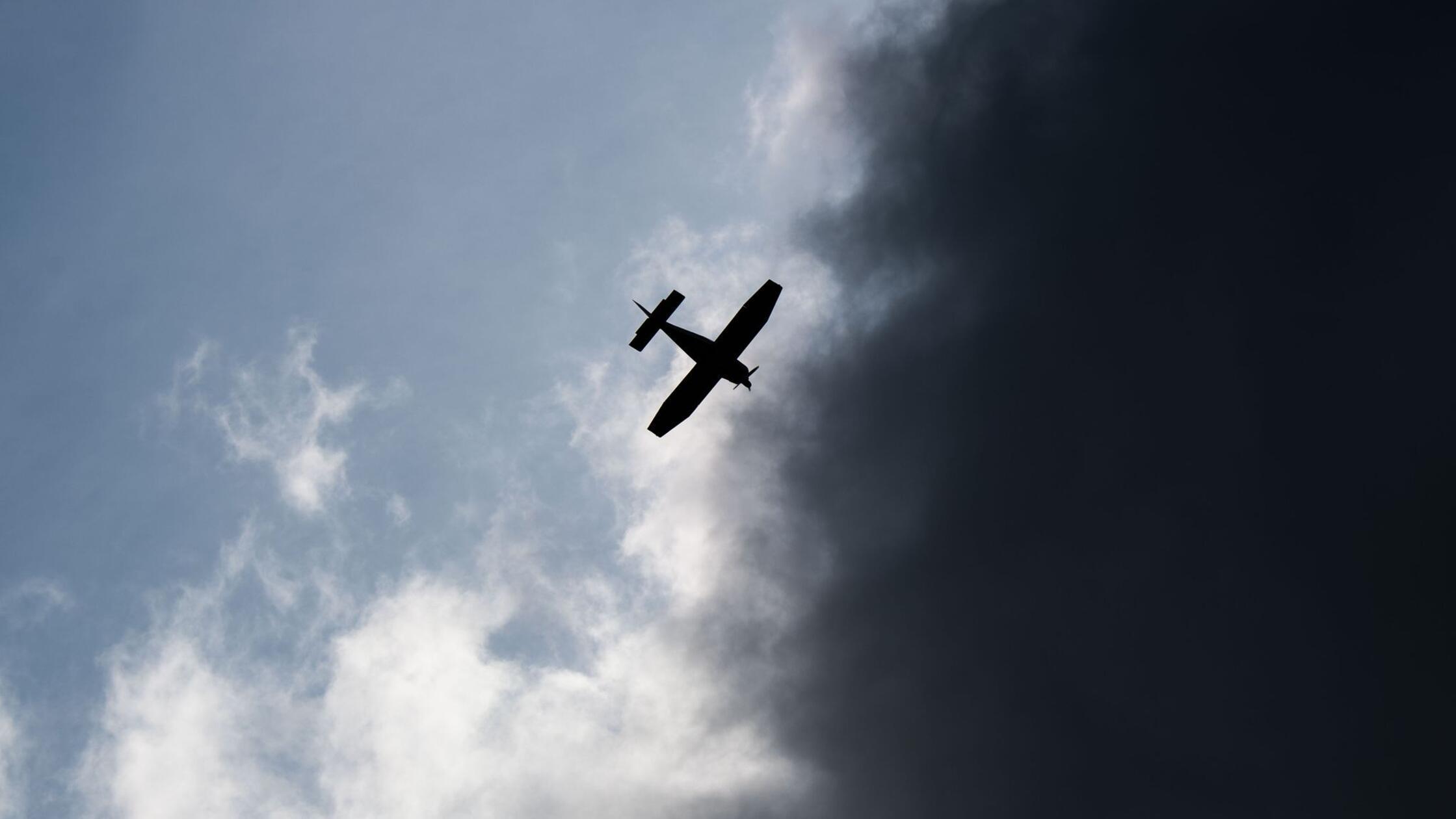 Ein Kleinflugzeug fliegt vor dunklen Wolken im Lan
