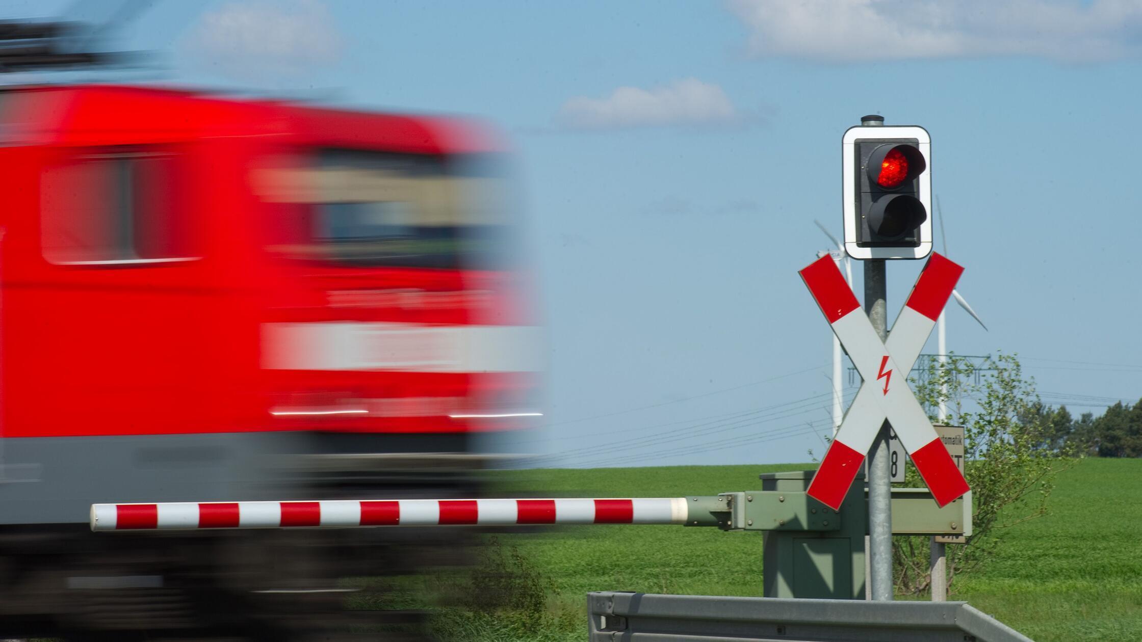 Ein Zug fährt an einem geschlossenem Bahnübergang 