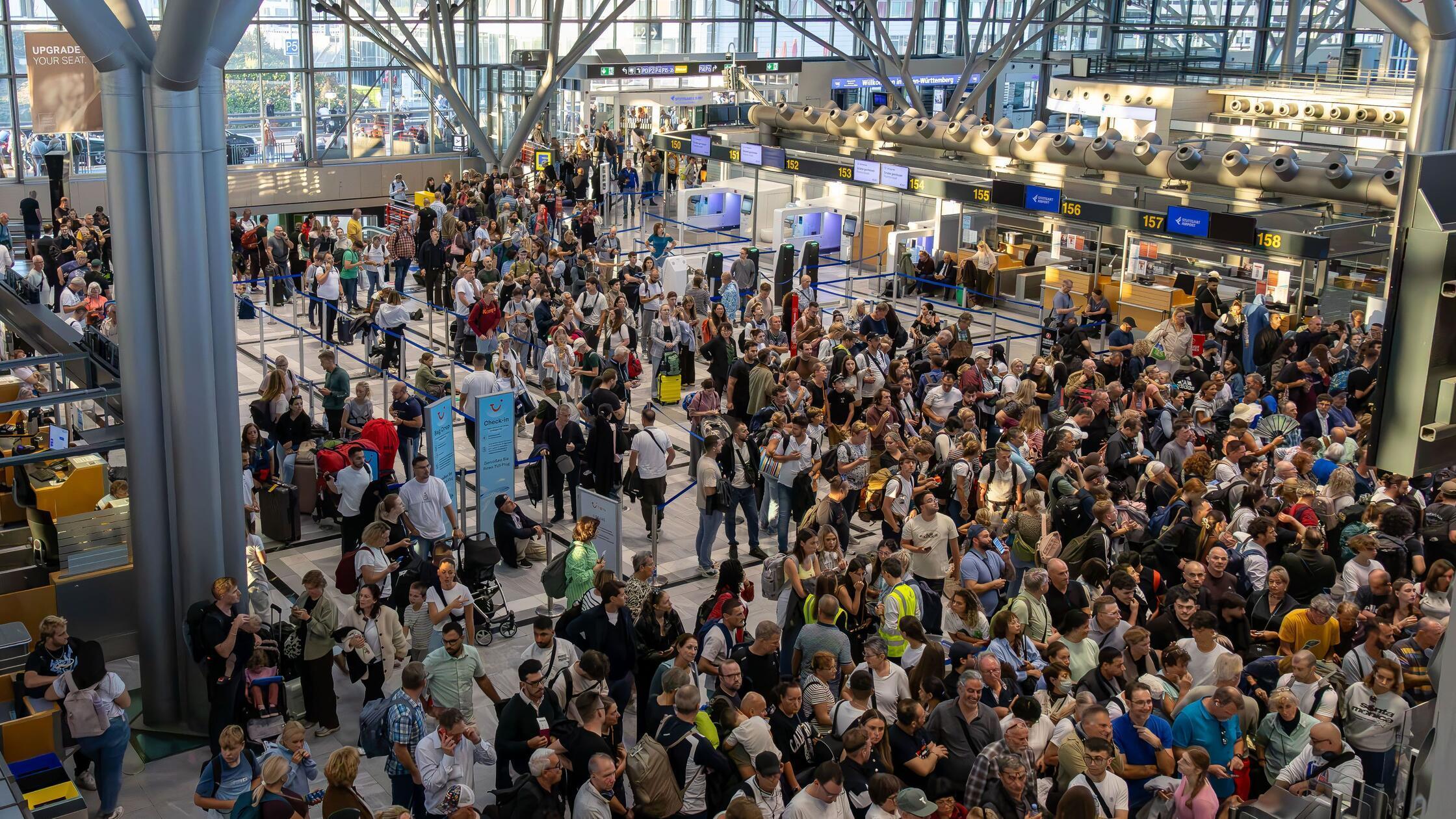 Zahlreiche Reisende stehen in einer Halle auf dem 