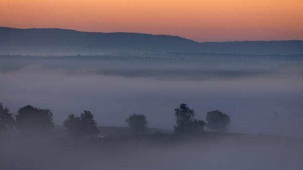 Ein Auto fährt kurz vor Sonnenaufgang im Morgenneb