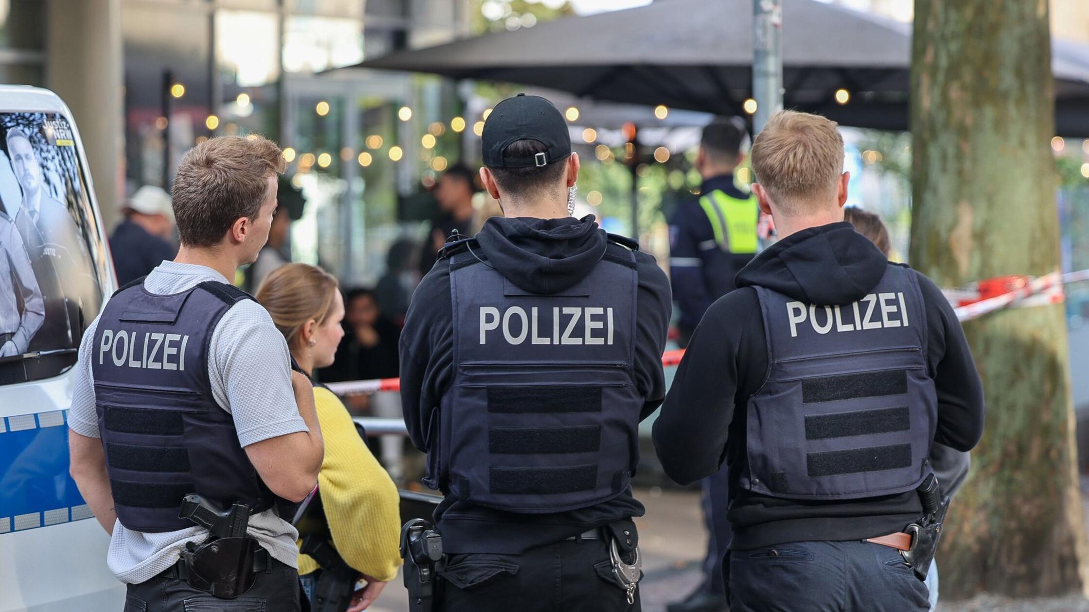 Polizisten stehen vor einem Absperrband. Zwei Unbe