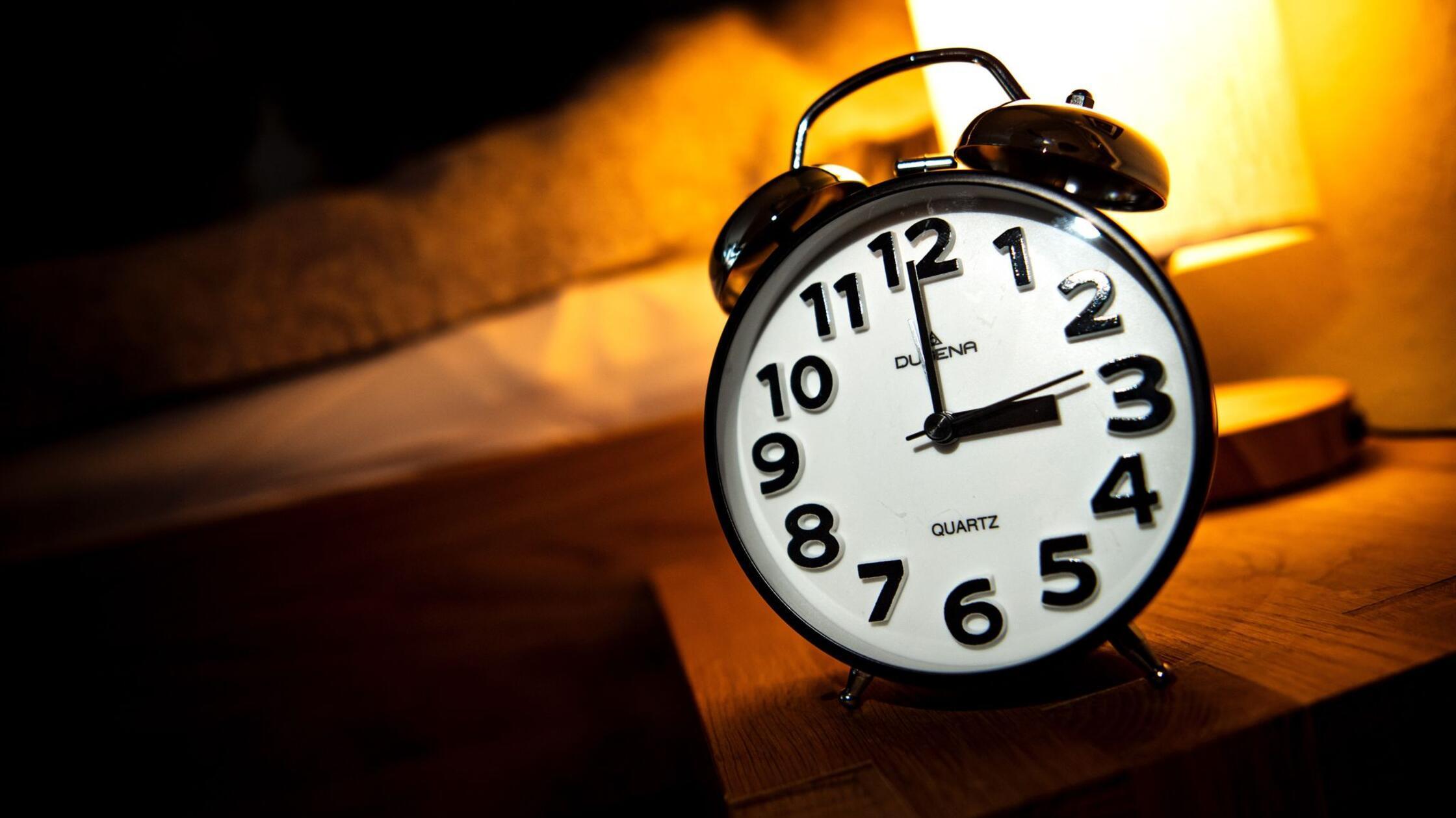 ILLUSTRATION - Eine Uhr steht neben einem Bett. Am