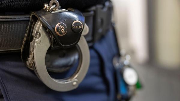 Eine Handschelle hängt am Gürtel eines Polizisten.