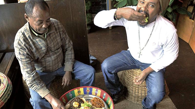 Hier heißt es herzhaft zugreifen und lustvoll stopfen: Wie in Äthiopien üblich, wird mit den Fingern gegessen. Besitzer Endale Mekuria (rechts) macht’s vor.