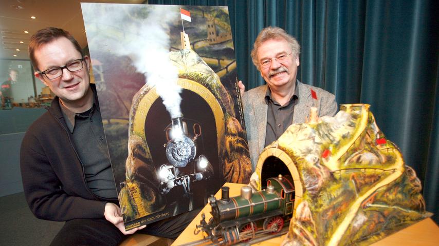 Grafikdesigner Udo Bernstein und Dr. Helmut Schwarz präsentieren das Plakat aus dem Jahr 2010 mit dem Motiv: "Eisenbahn mit Tunnelblick"
