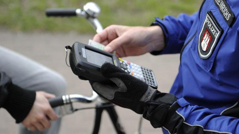 Ein Hamburger Polizist schreibt einen Radfahrer auf, der eine rote Ampel missachtet hat. Die Hansestadt leitet die Bund-Länderkommission, die den Bußgeldkatalog überarbeitet.