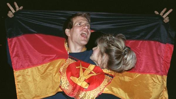 Hammer und Zirkel zweckentfremdet: Mit einer DDR-Flagge freuen sich zwei junge Ostberliner am 2.10.1990 über die bevorstehende deutsche Wiedervereinigung.