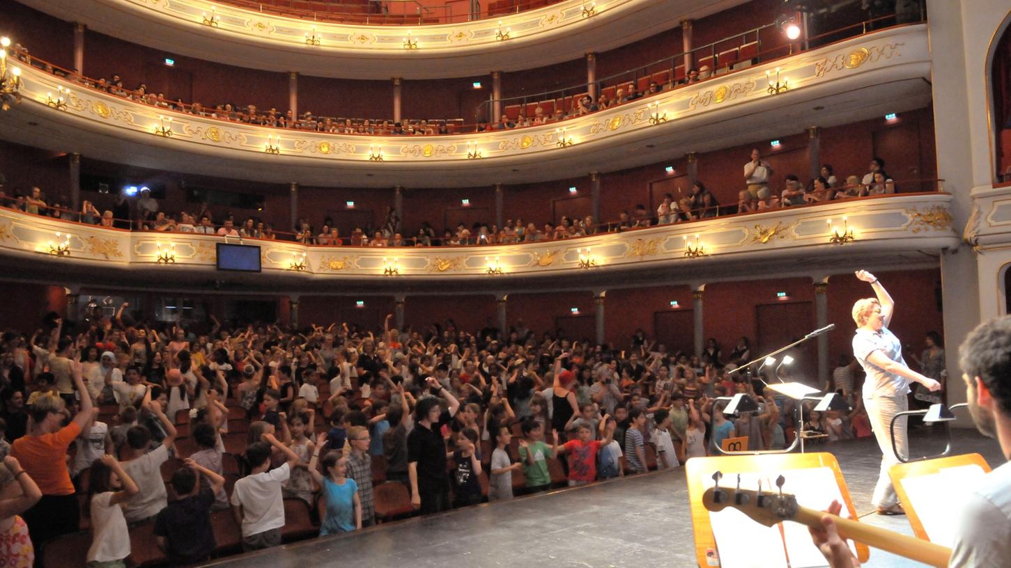 Am Meistersinger-Tag spielte sich fast alles nicht auf der Bühne im Opernhaus, sondern im Parkett ab. Denn dort saßen rund 500 Grundschüler aus Nürnberg und Umgebung. Wobei, gesessen haben sie kaum: Zu jedem Lied, das sie unter Anleitung von Heike Henning (re. auf der Bühne) sangen, zeigten sie eine passende Choreografie. Am Meistersinger-Tag spielte sich fast alles nicht auf der Bühne im Opernhaus, sondern im Parkett ab. Denn dort saßen rund 500 Grundschüler aus Nürnberg und Umgebung. Wobei, gesessen haben sie kaum: Zu jedem Lied, das sie unter Anleitung von Heike Henning (re. auf der Bühne) sangen, zeigten sie eine passende Choreografie.