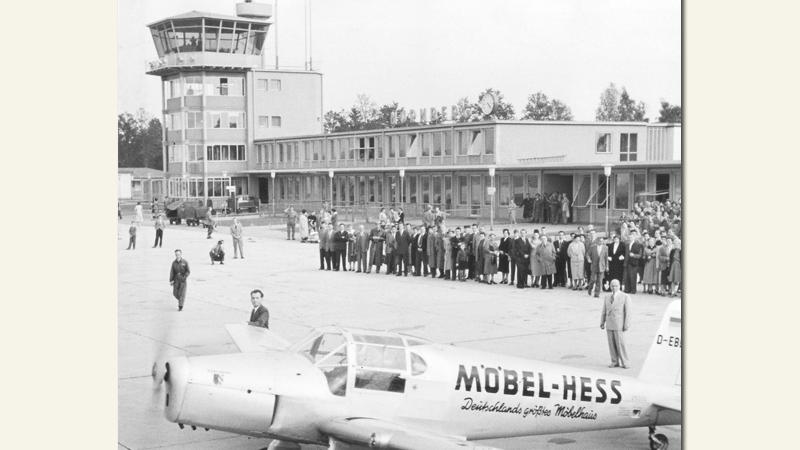 1955 wurde der Nürnberger Flughafen als erster neugebauter Verkehrsflughafen der Bundesrepublik im Knoblauchsland nördlich der Stadt eröffnet. Seitdem wuchs der Strom der Reisenden kontinuierlich – und der Flughafen mit ihm. 

Abheben konnten die Menschen aus dem Großraum allerdings schon früher — seit 1919 diente der einstige Militärlandeplatz in Fürth-Atzenhof als Flugplatz, ehe er vom Flughafen Marienberg abgelöst wur­de — dem ersten Airport auf Nürnber­ger Grund. Auf dem Bild tauft der hiesige Aero-Club eine Maschine auf den Namen «Nürnberg». 