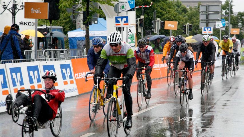 Während die Radfahrer sich durch den Regen kämpfen, bleiben die Zuschauer unter ihren Schirmen.