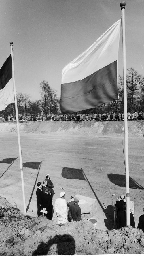 Grundsteinlegung im Luitpoldhain mit drei Hammerschlägen im März 1961. Die Ehrengäste, die zu Hunderten am gegenüberliegenden Rand der Baugrube stehen, lauschen den Rednern.
