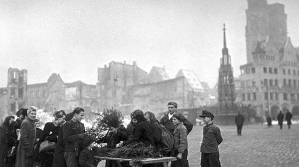 Nach Beginn des Zweiten Weltkrieges gab es einige Jahre lang keinen Christkindlesmarkt. Dieses Bild entstand 1947 und zeigt den Verkauf von Tannenzweigen auf dem Hauptmarkt. Im Hintergrund sind der Schöne Brunnen und die Türme der Sebalduskirche zu sehen. In diesem Jahr kehrte auch Friedrich Bröger aus der englischen Kriegsgefangenschaft zurück. So konnte er den Prolog für das Christkind im kommenden Jahr verfassen.
