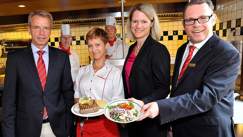Direktorin Sarah Cordes (Mitte), Betriebsleiter Ferdinand Kopsch (rechts) und Stephan von Bülow (links), Vorstand der Block House Restaurantbetriebe AG, präsentieren gemeinsam mit einer fröhlichen Servicekraft ein Steak-Gericht.
