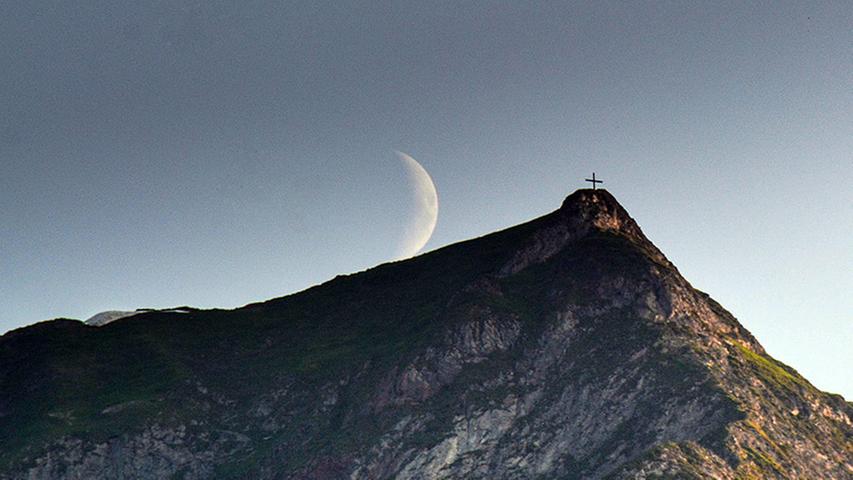 Der Mond steht über einem Gipfelkreuz in Warth-Schröcken. Selbst zu später Stunde ist das Panorama hier beeindruckend.