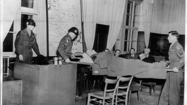 Der Einsatzgruppen-Prozess war der neunte von zwölf Nürnberger Nachfolgeprozessen. SS-Brigadeführer Otto Rasch, der für das Massaker von Babyn Jar und dem Tod von über 30.000 Juden verantwortlich gemacht wurde, litt bei den Verhandlungen an Parkinson. Von amerikanischen Soldaten wird er auf einer Bahre zur Vernehmung in eigener Sache in den Gerichtssaal getragen.