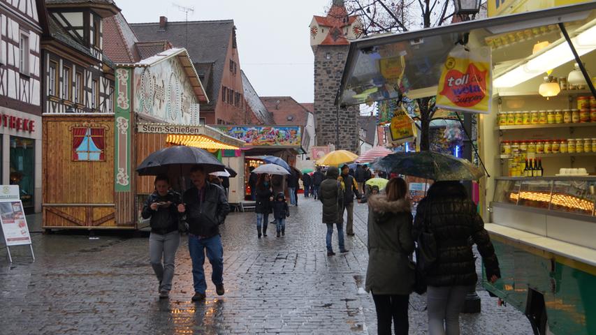 Bei Nacht in romantische Lichter getaucht zeigt sich der Jahrmarkt bei Tag eher grau: Das trübe Novemberwetter treibt die Kirchweihfans tief unter ihre Regenschirme.