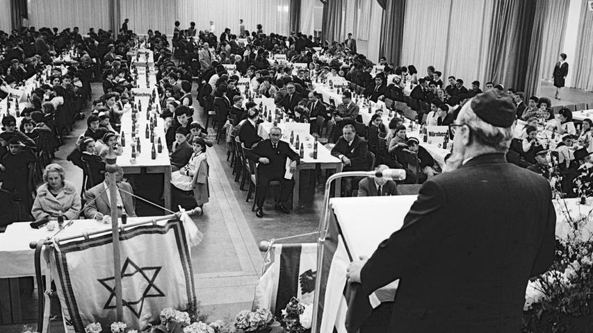 Rabbiner H. I. Grünwald aus München spricht im Messehaus zu 500 jüdischen Kindern, die ihre Fahnen (im Vordergrund) mitgebracht haben. Der Kindertag nahm mit Gesang und Rezitation einen frohen Auftakt. Die Lehrer der Kinder waren dabei.  Hier geht es zum Artikel: "Ein Festtag für jüdische Kinder"