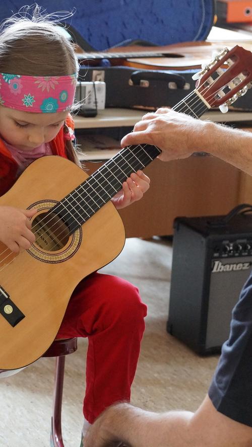 Und Gitarrenlehrer Guenter Zollfrank zeigt einer Sechsjährigen, wie sie die Gitarre richtig hält, um spielen zu können.