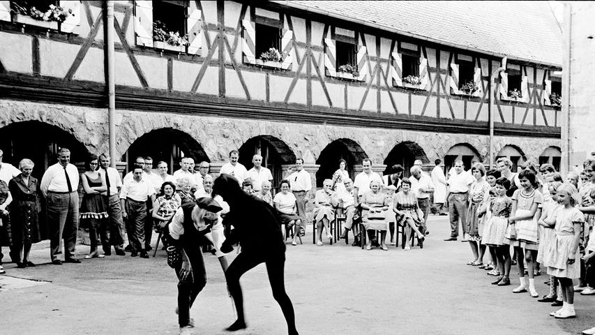 Kinder tanzen und spielen vor dem Oberbürgermeister (ganz links) und den Stadträten im stimmungsvollen Hof der Burg Hoheneck. Ein Dank für manches finanzielle Opfer der Stadt. Hier geht es zum Artikel: 20. Juli 1964: Mit dem "Moritz" auf dem Main