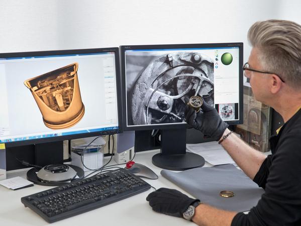 Der Restaurateur und Historiker Roland Schewe sitzt mit der Henlein-Uhr in der Hand vor zwei Bildschirmen mit detaillierten Großaufnahmen der Uhr. Links ist eine 3D-Computer-Tomographie zu sehen, rechts eine Aufnahme im sogenannten Streifenlichtverfahren.