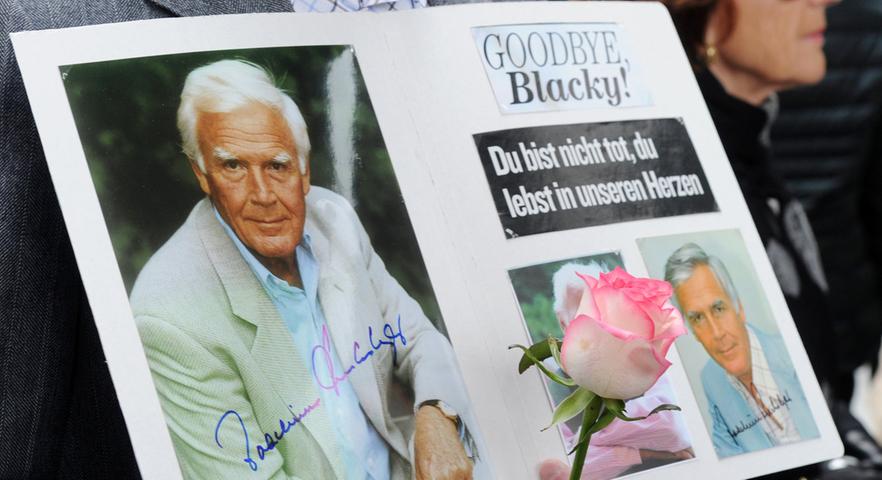 Ein Fan hält ein selbstgemachtes Plakat mit Fotos und der Aufschrift "Goodbye Blacky! Du bist nicht tot, du lebst in unseren Herzen" und eine Rose in den Händen.