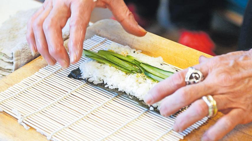 Das Algenblatt namens „Nori“ liegt vor Ihnen, darauf drücken Sie eine Zentimeterschicht Sushi-Reis, lassen aber etwa einen Zentimeter am oberen Rand frei. Jetzt mit einem Finger eine Spur Wasabi auf den Reis streichen, nicht zu viel Gurke oder eine andere Füllung in die Mitte des Blattes legen.
