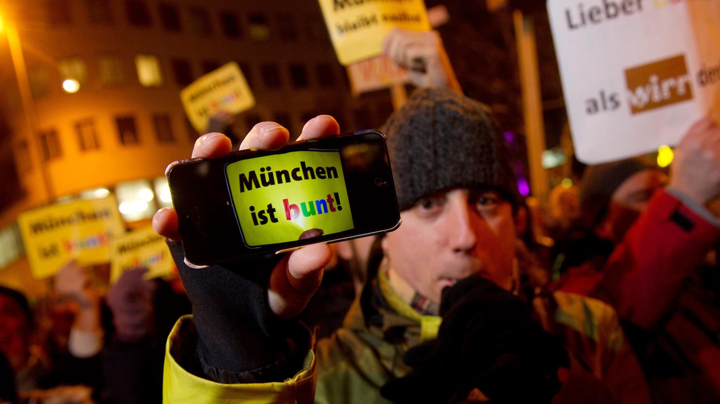 Ein Demonstrant hält am Montagabend in München bei einer Demonstration gegen die islamkritische Bagida-Bewegung sein Handy, das den Schriftzug "München ist bunt!" zeigt, in die Kamera.