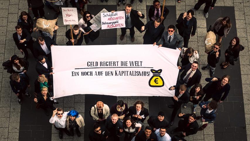 Demonstranten halten am 25.04.2015 in Nürnberg (Bayern) das Banner "Geld  regiert die Welt. Ein Hoch auf den Kapitalismus" in den Händen. Nürnberger  Jugendorganisationen zogen mit ihrer Satire-Demonstration durch die Nürnberger  Innenstadt und kritisierten damit insbesondere die Geld-Politik. Foto: Nicolas  Armer/dpa +++(c) dpa - Bildfunk+++