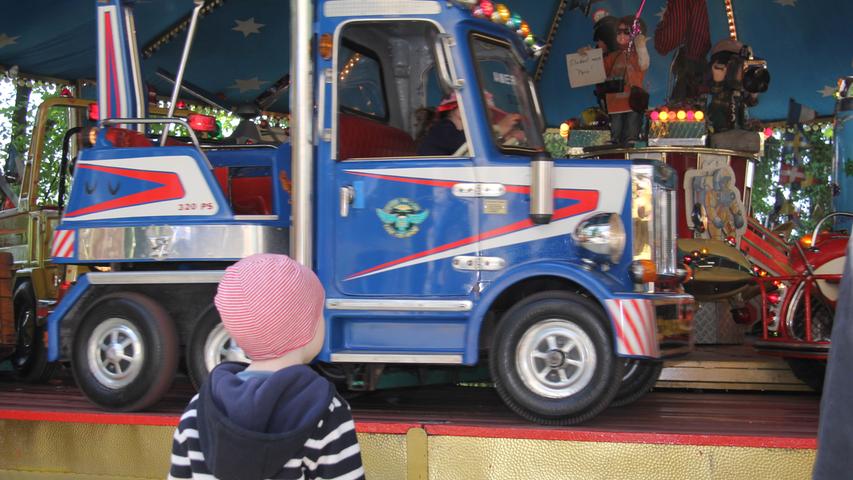 Sehnsüchtig blickt hier ein kleiner Besucher auf die sich schnell im Kreis drehenden Autos des Kinderkarussells ...