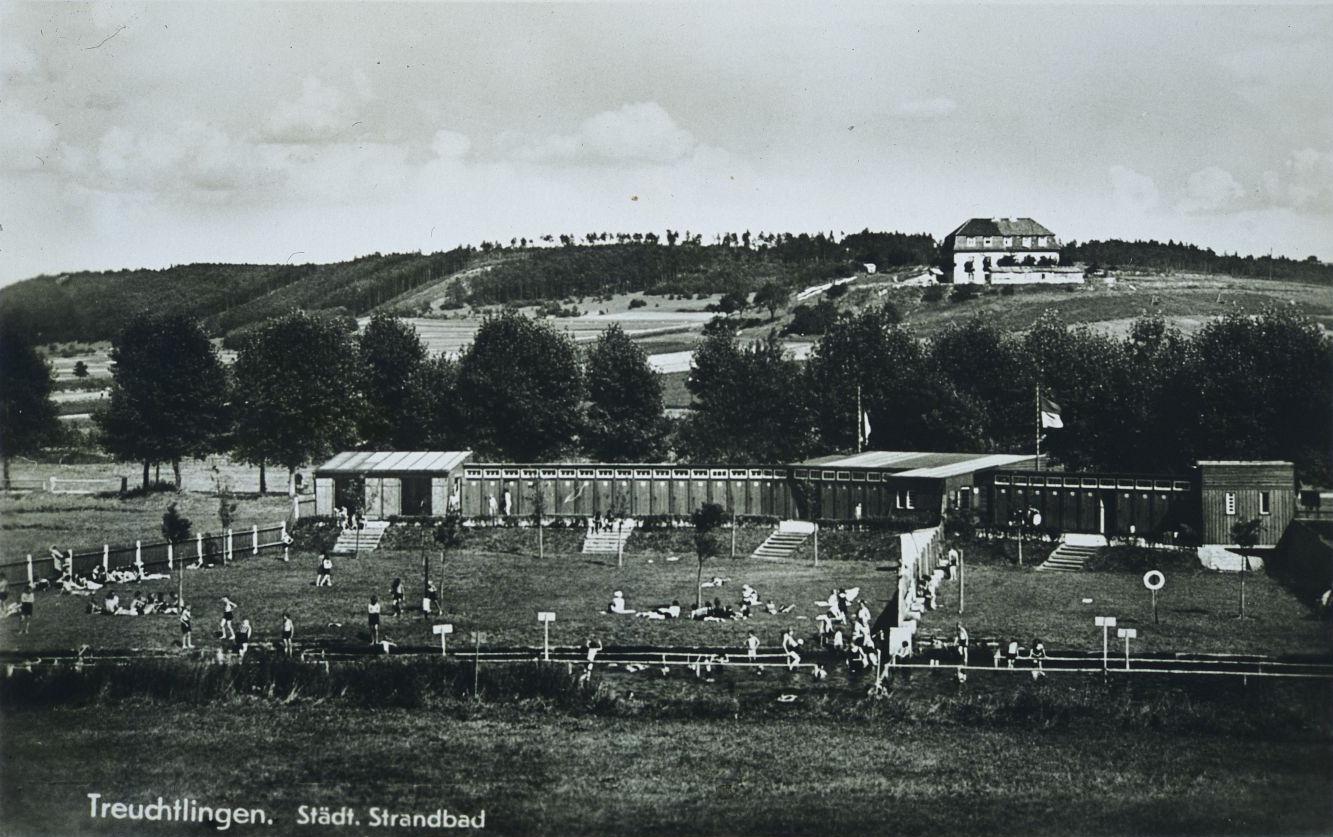 In der 1950er Jahren waren die Liegewiesen und Kabinen des Treuchtlinger Flussbads noch streng getrennt. Die Städtische Badeanstalt war von einem Zaun eingefasst, und zum Weg hin gab es eine hohe Bretterwand gegen neugierige Blicke. Parallel zur Altmühl verlief ein langgezogenes Holzgebäude mit der Kasse und den Umkleiden. Einzelkabinen kos­te­ten extra. Über Sicherheit und Ordnung wachten die Bademeister Reichl und Hüttinger. An der Kasse standen ihre Frauen, die Kinder reinigten die Kabinen. Zur Stärkung gab es Brezen und „Amerikaner“ sowie furchtbar süße Himbeer- und giftgrüne Waldmeister-Limonade. Bei Hochwasser war die Altmühl zum Baden gesperrt. Ebenso bei langen Hitzeperioden, wenn das Wasser genauso himbeerrot wie die Limonade wurde und die Kinder nach dem Baden Hautausschlag bekamen. Am sandigen Flussboden ertauchten die Jugendlichen in den Nachkriegsjahren auch immer wieder militärische Hinterlassenschaften wie Munition, Handgranaten und nicht explodierte Brandstabbomben. Das Gebäude im Bildhintergrund am Hang des Galgebucks ist übrigens die ehemalige Ausflugsgaststätte Ukat. Dort gab es Küken, die die Treuchtlinger Kinder im Auftrag ihrer Eltern zur Aufzucht kauften, sowie sonntags Kaffee, Kuchen und Musik vom Schifferklavier. Zur kompletten Geschichte des Flussbads geht es hier.