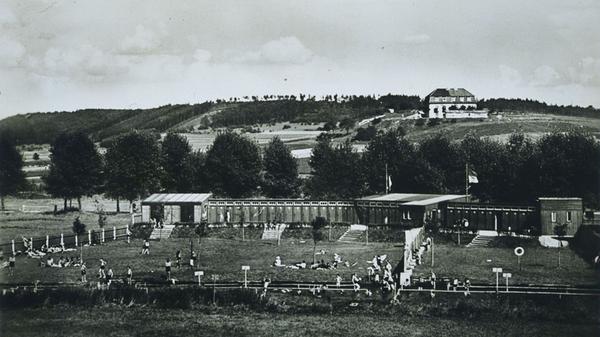 In der 1950er Jahren waren die Liegewiesen und Kabinen des Treuchtlinger Flussbads noch streng getrennt. Die Städtische Badeanstalt war von einem Zaun eingefasst, und zum Weg hin gab es eine hohe Bretterwand gegen neugierige Blicke. Parallel zur Altmühl verlief ein langgezogenes Holzgebäude mit der Kasse und den Umkleiden. Einzelkabinen kosteten extra. Über Sicherheit und Ordnung wachten die Bademeister Reichl und Hüttinger. An der Kasse standen ihre Frauen, die Kinder reinigten die Kabinen. Zur Stärkung gab es Brezen und „Amerikaner“ sowie furchtbar süße Himbeer- und giftgrüne Waldmeister-Limonade. Bei Hochwasser war die Altmühl zum Baden gesperrt. Ebenso bei langen Hitzeperioden, wenn das Wasser genauso himbeerrot wie die Limonade wurde und die Kinder nach dem Baden Hautausschlag bekamen. Am sandigen Flussboden ertauchten die Jugendlichen in den Nachkriegsjahren auch immer wieder militärische Hinterlassenschaften wie Munition, Handgranaten und nicht explodierte Brandstabbomben. Das Gebäude im Bildhintergrund am Hang des Galgebucks ist übrigens die ehemalige Ausflugsgaststätte Ukat. Dort gab es Küken, die die Treuchtlinger Kinder im Auftrag ihrer Eltern zur Aufzucht kauften, sowie sonntags Kaffee, Kuchen und Musik vom Schifferklavier. Zur kompletten Geschichte des Flussbads geht es hier.