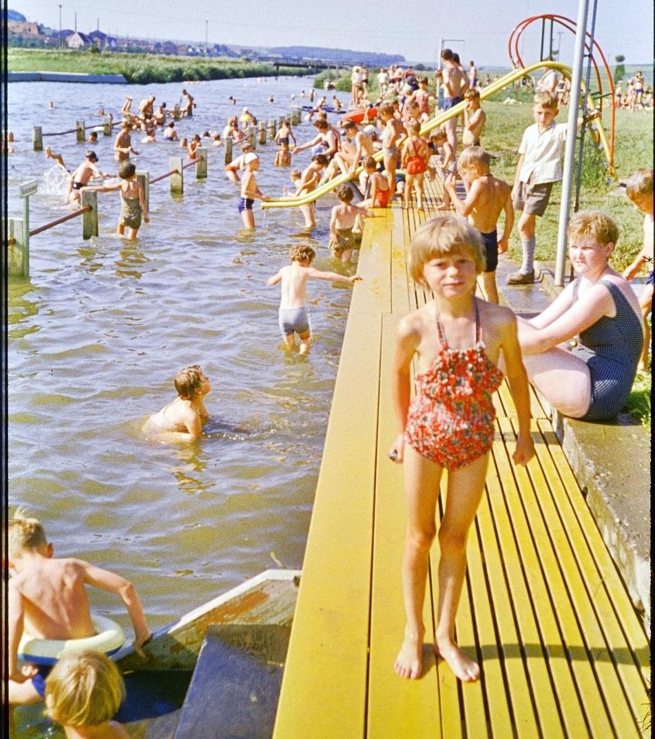 In den 1960er Jahren war das Treuchtlinger Flussbad sommerlicher Tummelplatz für Groß und Klein. Für die Teenager war die Badeanstalt der Treffpunkt schlechthin zum Kennenlernen und Flirten. Neben der kleinen Metallrutsche, an der man sich bei Hitze stets den Hintern verbrannte, gab es einen hölzernen Sprungturm mit Zwei- und Drei-Meter-Brett, auf dem die Jungs die Mädchen zu beeindrucken versuchten. Im Bildhintergrund erkennt man die durch Geländer abgetrennten Badezonen für Kinder, Nichtschwimmer und Schwimmer sowie die bis 1966 noch hölzerne „Promenadenbrücke“. Zur kompletten Geschichte des Flussbads geht es hier.