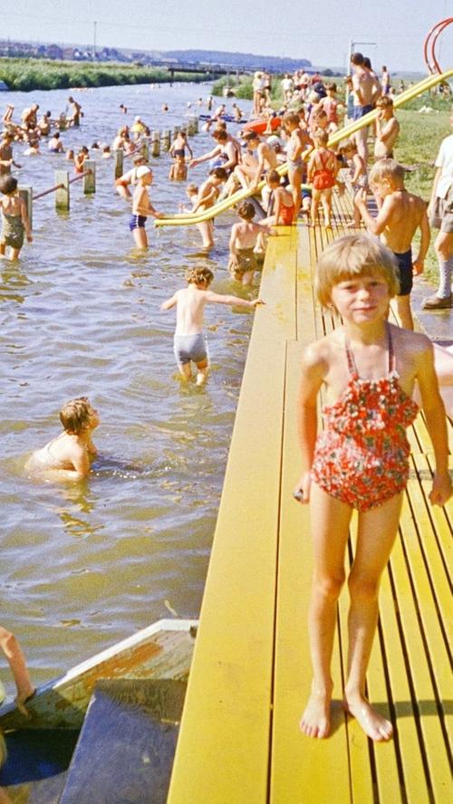 In den 1960er Jahren war das Treuchtlinger Flussbad sommerlicher Tummelplatz für Groß und Klein. Für die Teenager war die Badeanstalt der Treffpunkt schlechthin zum Kennenlernen und Flirten. Neben der kleinen Metallrutsche, an der man sich bei Hitze stets den Hintern verbrannte, gab es einen hölzernen Sprungturm mit Zwei- und Drei-Meter-Brett, auf dem die Jungs die Mädchen zu beeindrucken versuchten. Im Bildhintergrund erkennt man die durch Geländer abgetrennten Badezonen für Kinder, Nichtschwimmer und Schwimmer sowie die bis 1966 noch hölzerne „Promenadenbrücke“. Zur kompletten Geschichte des Flussbads geht es hier .