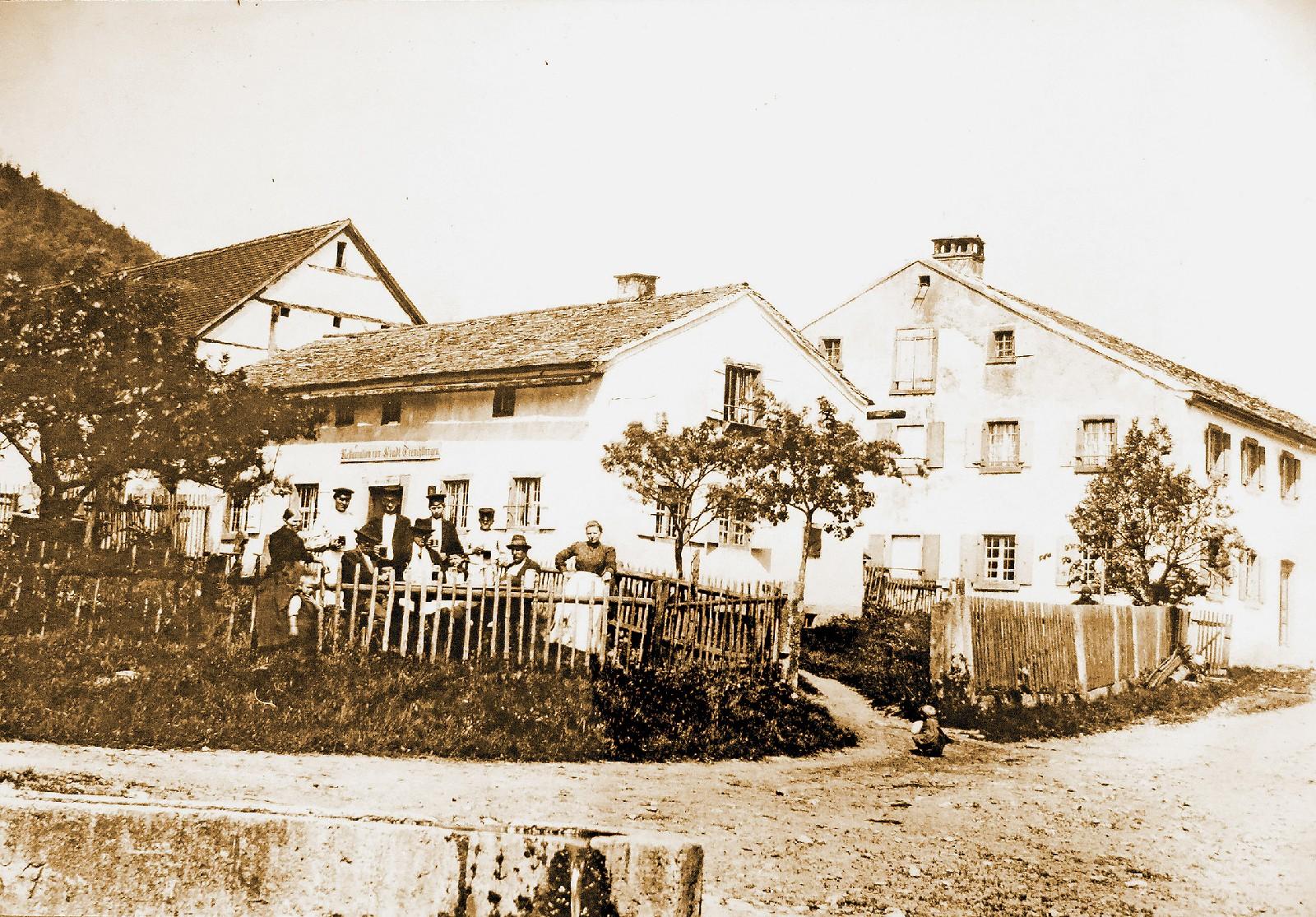 Dieses Foto zeigt die ursprüngliche Wirtschaft in Gstadt, die in dieser Form bis zum Jahr 1905 betrieben wurde. Inhaber war Georg Meyer. Das Gebäude ist heute noch in Familienbesitz und wird als Wohnhaus genutzt. Links neben der Wirtschaft ist die dazugehörige Scheune zu sehen, rechts das Anwesen Jungmeyer. Der Bergrücken links im Hintergrund ist der Patrichberg. Mehr zu der Geschichte des Anwesens lesen Sie hier.