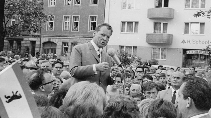 Willy Brandt in der Nürnberger Innenstadt: von dem fahrbaren Rednerpult aus spricht er zu den schätzungsweise 2000 Menschen, die sich auf dem Hallplatz eingefunden haben. Neben Brandt stehen auf dem Rednerpult OBM Dr. Urschlechter, Bgm. Franz Haas und die Abgeordneten Käte Strobel und G. Kurlbaum.Hier geht es zum Artikel vom 23. August 1965: Hart und steinig ist der Weg zur Macht