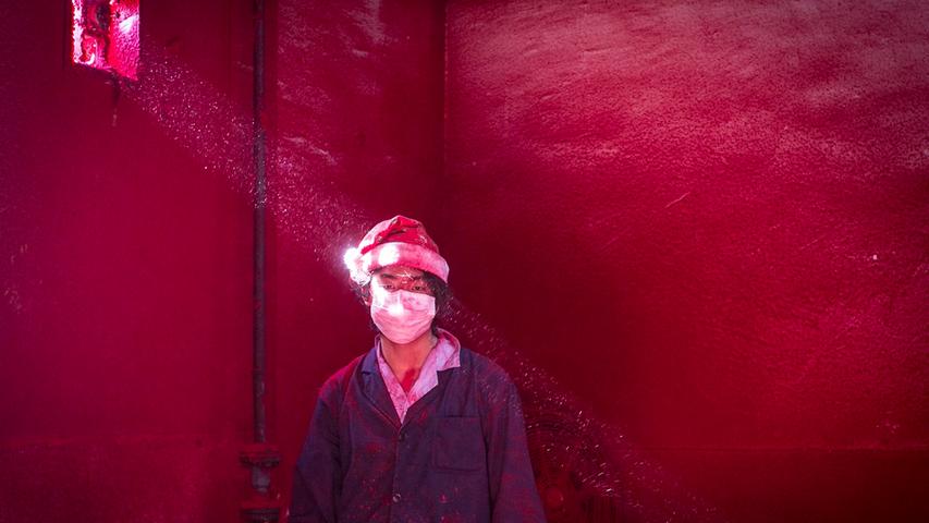 Wei, ein 19-jähriger chinesischer Arbeiter, hat eine Nikolausmütze auf. Er arbeitet in einer Fabrik, in der Weihnachtsartikel hergestellt werden. Er trägt sechs Atemmasken am Tag, die den Staub aus seinen Lungen halten sollen.