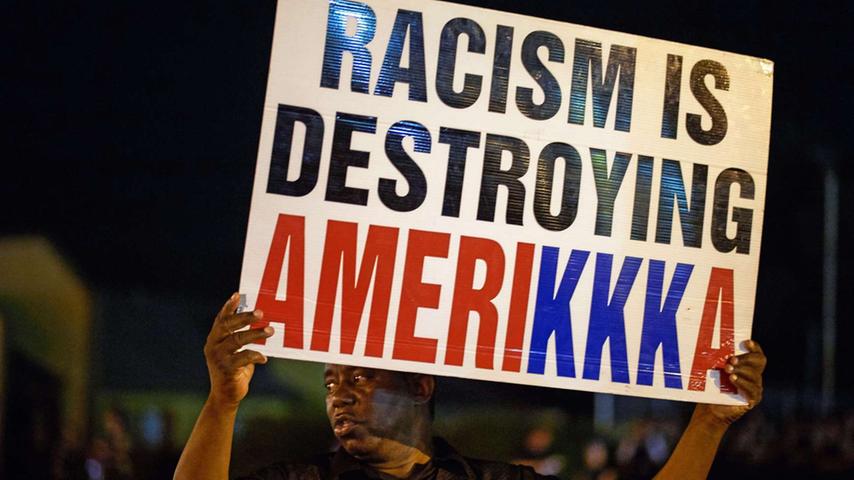 "Rassismus zerstört Amerika" heißt es auf dem Plakat, die drei KKK spielen auf den rechtsradikalen Ku-Klux-Klan an: Die Gegensätze zwischen Weiß und Schwarz brechen unter Obama erneut auf. Als bei mehreren Vorfällen weiße Polizisten schwarze Jugendliche erschießen, kommt es zu einer Debatte über Polizeigewalt, die in Demonstrationen und gewalttätigen Auseinandersetzungen mündet. Auch hier wird klar: Obamas Mission der Versöhnung ist gescheitert.